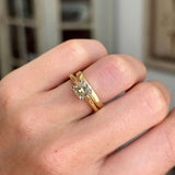 Vintage 1950s brown old-mine cut diamond solitaire engagement ring worn with a gold wedding band on a finger with a blurred background.