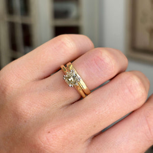 Vintage 1950s brown old-mine cut diamond solitaire engagement ring worn with a gold wedding band on a finger with a blurred background.
