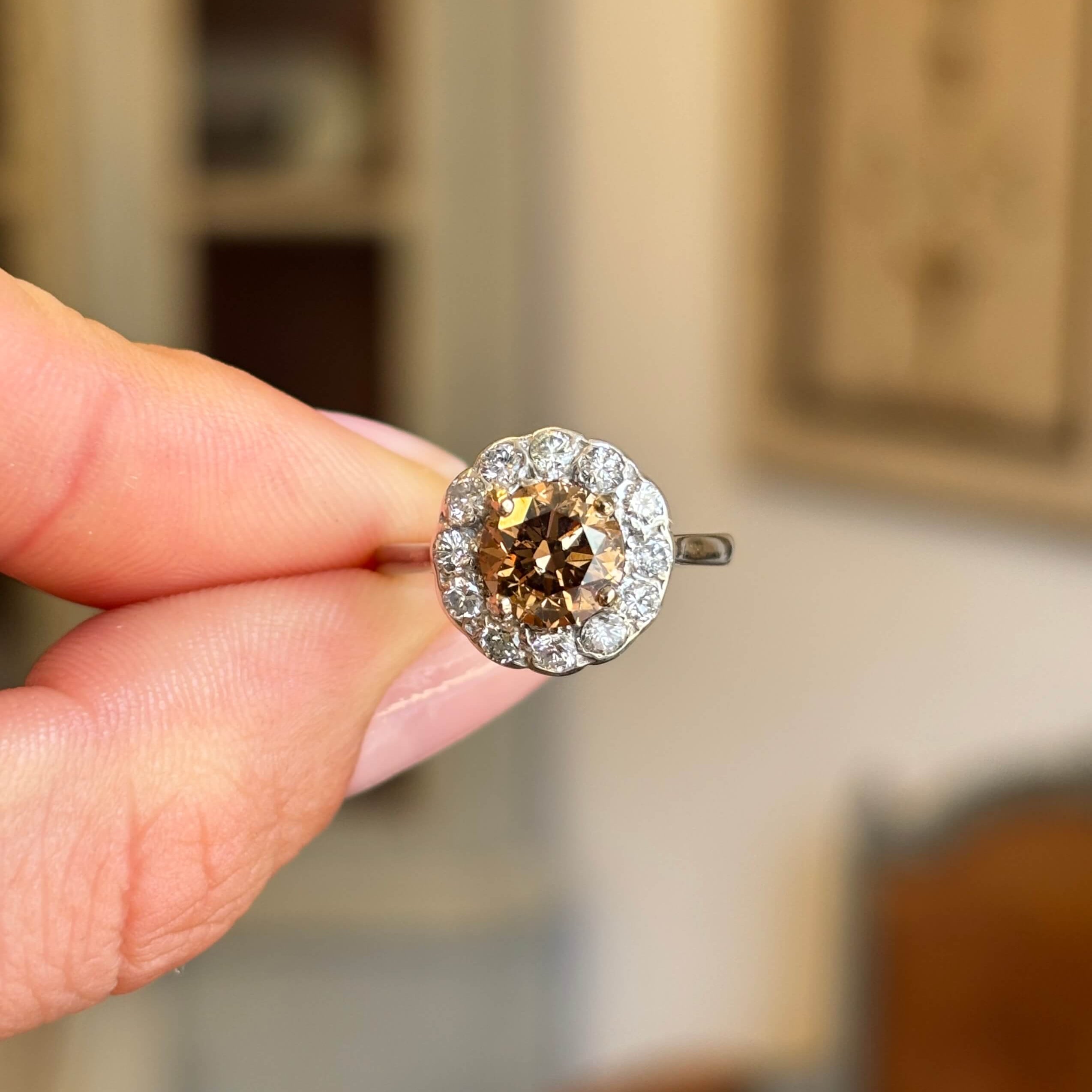 Vintage 1950s cinnamon brown diamond cluster engagement ring featuring a cinnamon brown diamond surrounded by a halo of diamonds, held by hand.