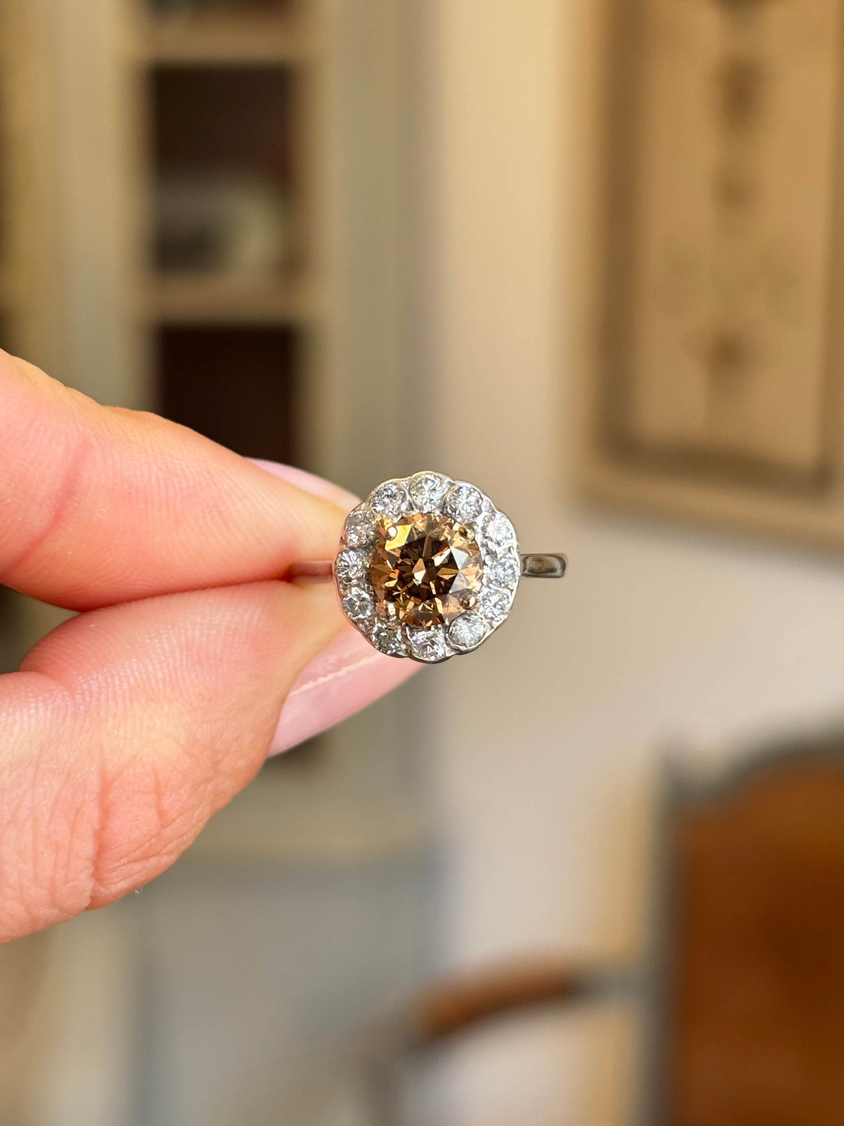 Vintage 1950s cinnamon brown diamond cluster engagement ring featuring a cinnamon brown diamond surrounded by a halo of diamonds, held by hand.