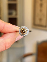 Vintage 1950s cinnamon brown diamond cluster engagement ring featuring a cinnamon brown diamond surrounded by a halo of diamonds, held by hand.