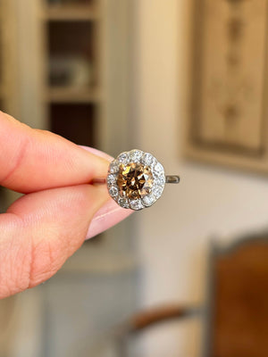 Vintage 1950s cinnamon brown diamond cluster engagement ring featuring a cinnamon brown diamond surrounded by a halo of diamonds, held by hand.