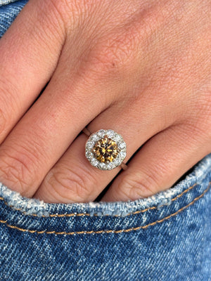 Vintage 1950s cinnamon brown diamond cluster engagement ring with a cinnamon brown diamond centre stone and diamond halo, worn on a hand.
