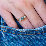 Vintage 1950s green sapphire and diamond three-stone engagement ring worn with hand resting in denim pocket.