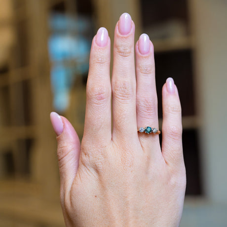 Vintage 1950s green sapphire and diamond three-stone engagement ring worn on hand.