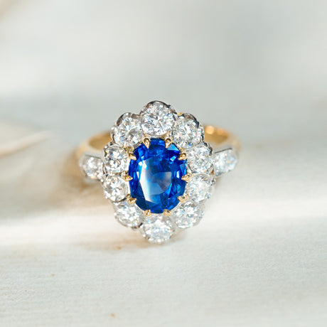 Vintage 1960s French sapphire and diamond cluster ring displayed on antique book pages with vivid sapphire centre stone.