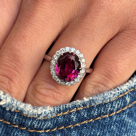 Vintage 1960s garnet and diamond cluster engagement ring with an oval garnet centre and diamond halo, worn on a hand.