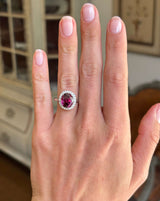 Vintage 1960s garnet and diamond cluster engagement ring with an oval garnet centre stone and diamond halo, displayed on a hand.