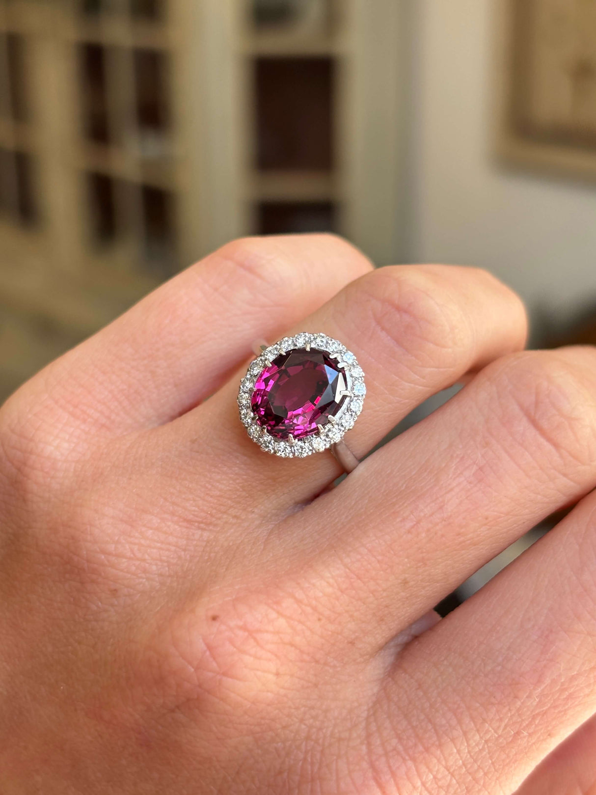 Vintage 1960s garnet and diamond cluster engagement ring featuring an oval garnet encircled by brilliant-cut diamonds, worn on a hand.