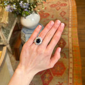 Vintage 1960s oval sapphire and diamond cluster ring worn on hand.
