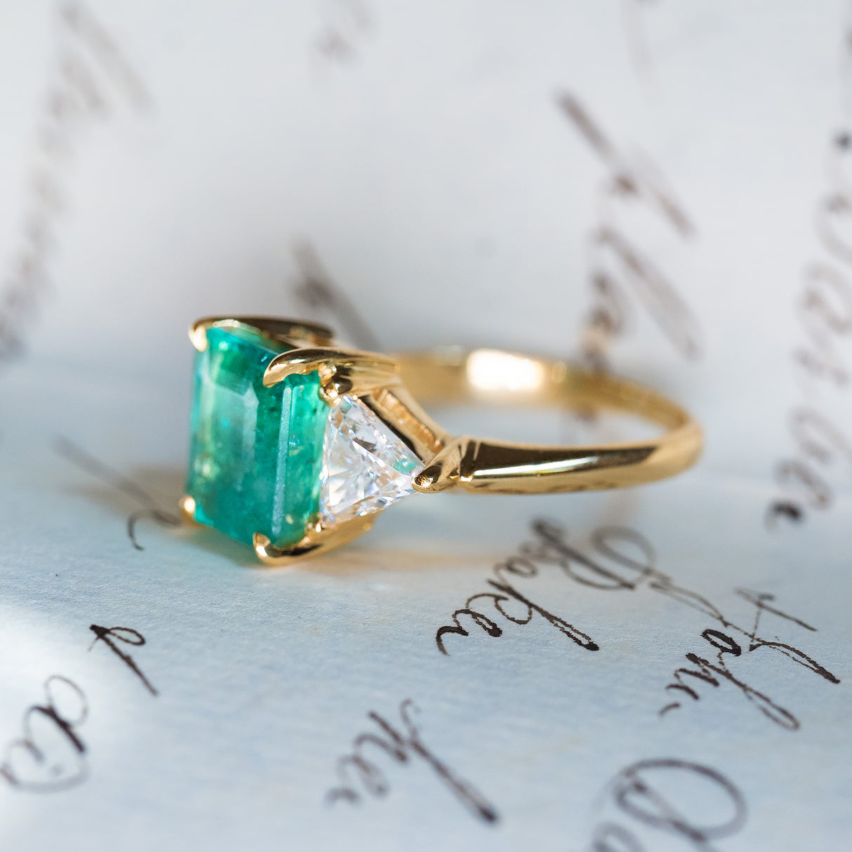 Vintage 1970s emerald and diamond three stone ring showing gold band and side diamond detail.