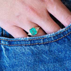 Close up of a vintage 1970s emerald and diamond three stone ring worn on hand with blue denim pocket detail.