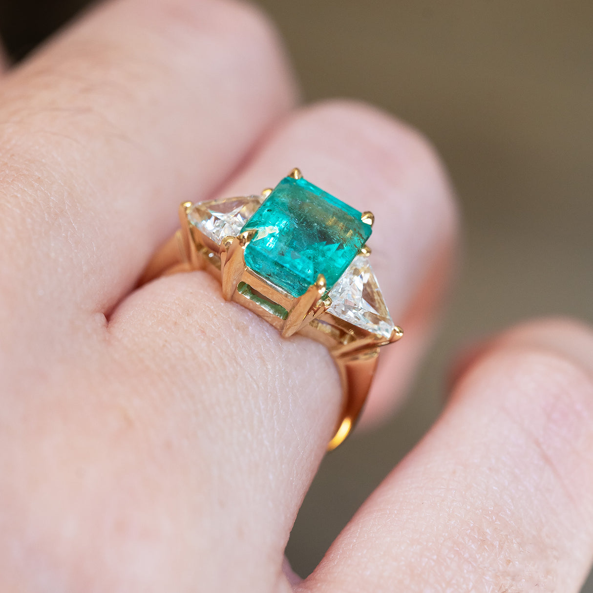 Vintage 1970s emerald and diamond three stone ring showing gold setting and diamond accents on hand.
