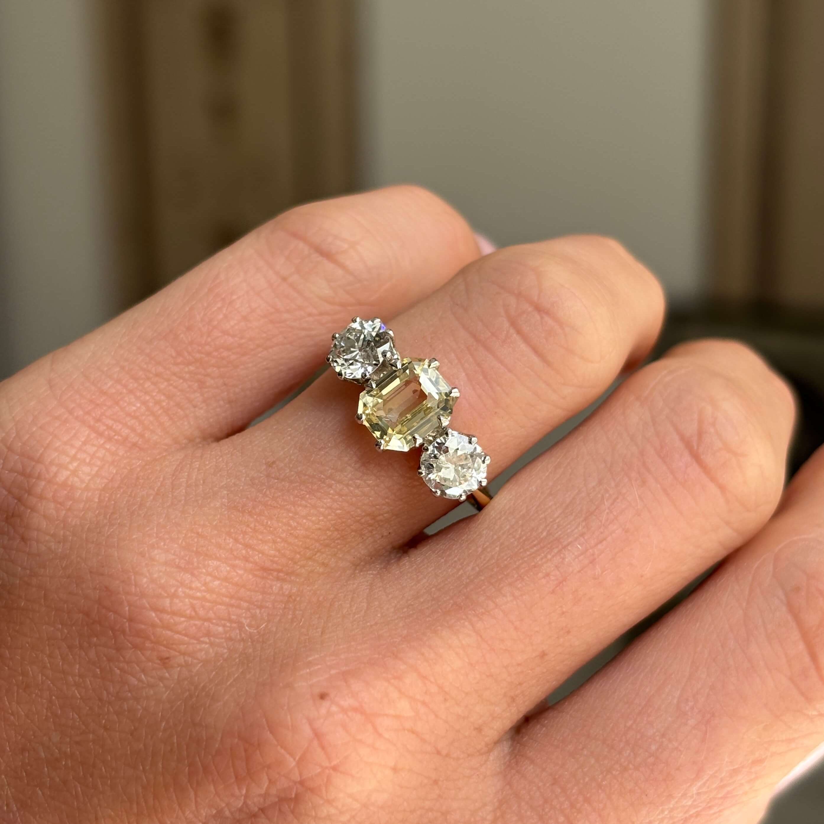 Vintage 1970s yellow sapphire and old-cut diamond three-stone engagement ring featuring a yellow sapphire centre stone and old-cut diamond accents, worn on a hand.