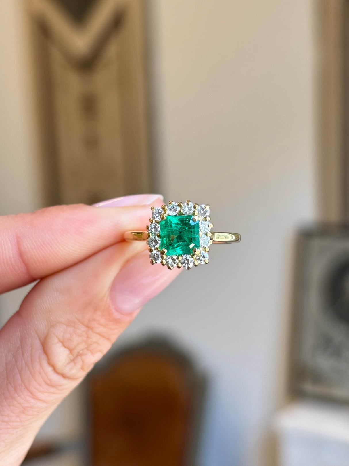 Vintage 1980s Colombian emerald and diamond cluster engagement ring featuring an emerald-cut Colombian emerald surrounded by a halo of brilliant-cut diamonds, held by hand.
