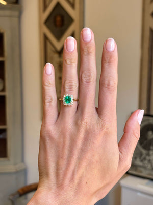 Vintage 1980s Colombian emerald and diamond cluster engagement ring with an emerald-cut Colombian emerald and diamond halo, displayed on a hand.