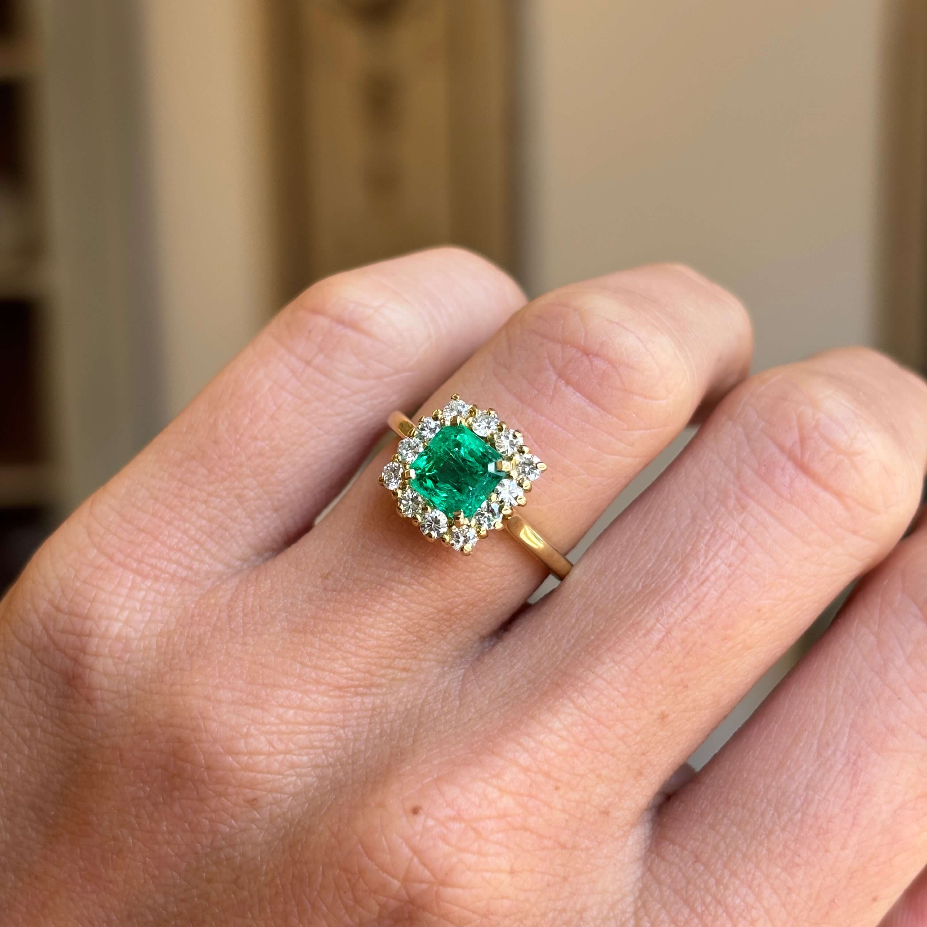 Vintage 1980s Colombian emerald and diamond cluster engagement ring featuring an emerald-cut Colombian emerald encircled by brilliant-cut diamonds, worn on a hand.