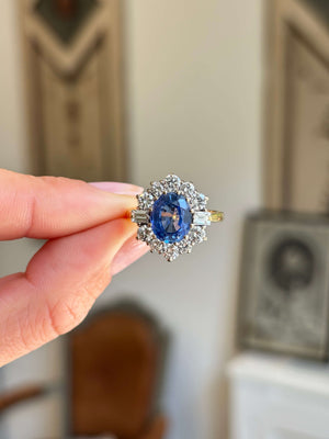 Vintage 1980s cornflower blue sapphire and diamond cluster ring featuring a cornflower blue sapphire surrounded by a halo of brilliant-cut diamonds, held by hand.