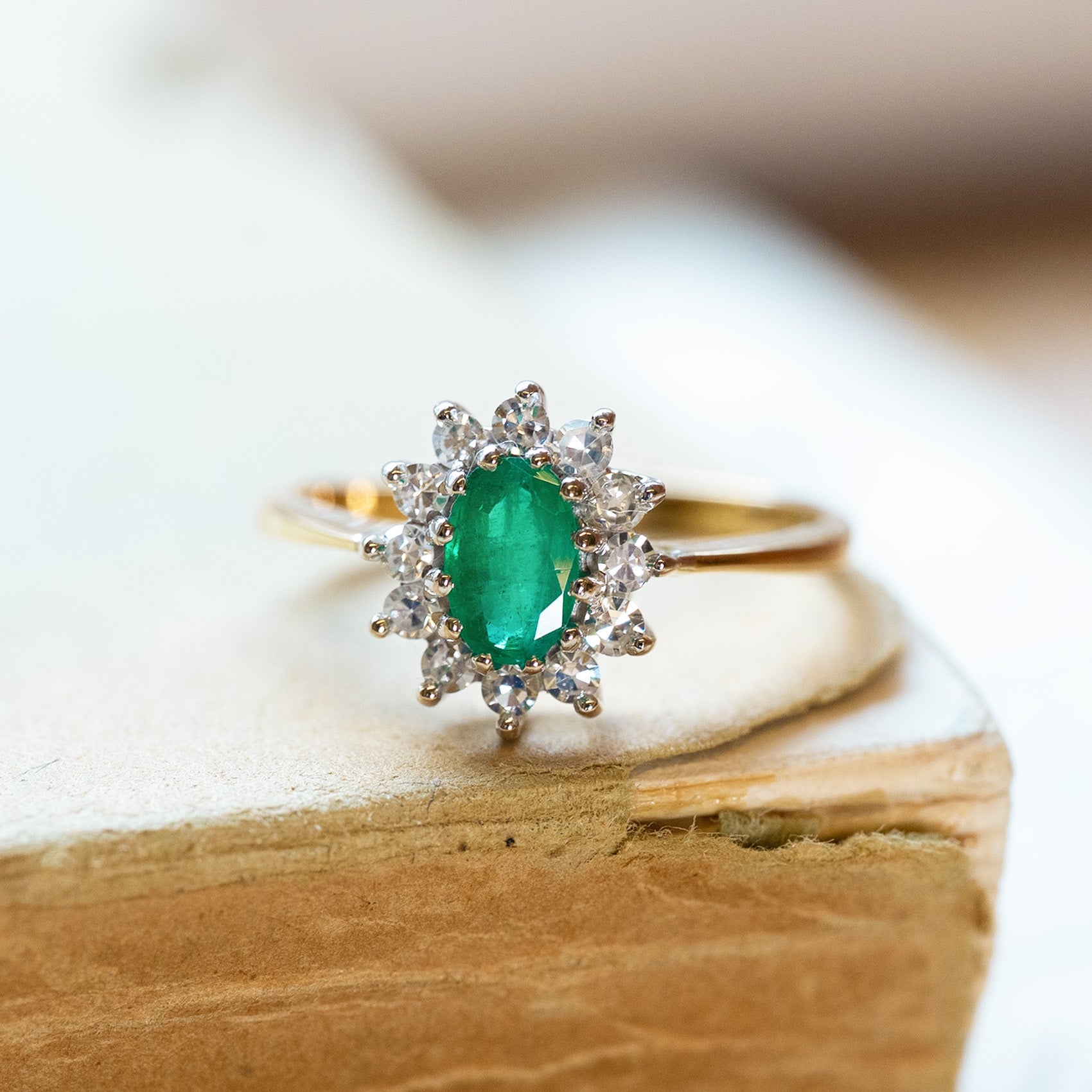 Vintage 1980s emerald and diamond cluster ring styled on aged book pages.