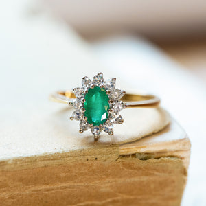 Vintage 1980s emerald and diamond cluster ring styled on aged book pages.