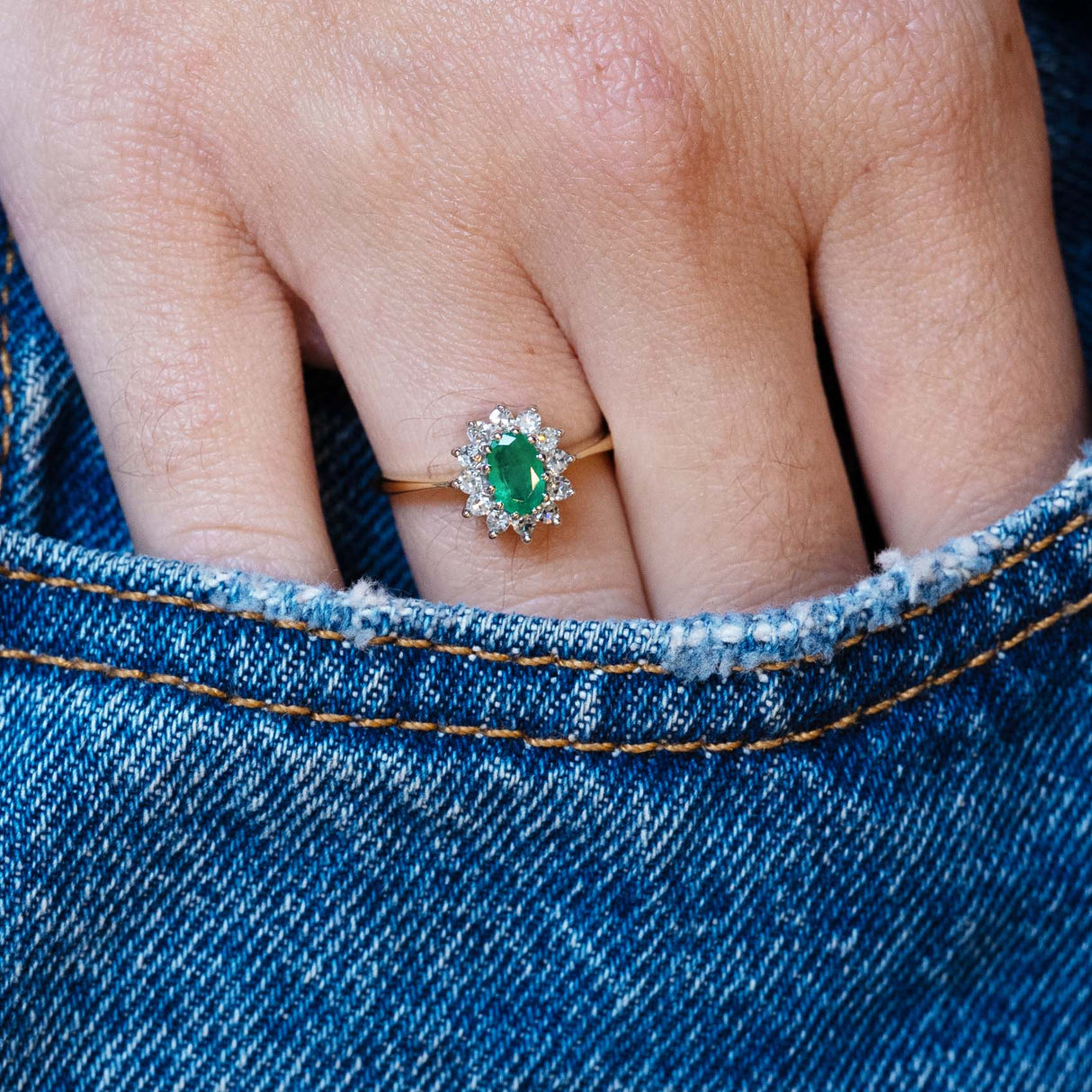 Vintage 1980s emerald and diamond cluster ring worn with hand resting in denim pocket.