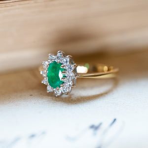 Vintage 1980s emerald and diamond cluster ring with bright oval emerald and diamond halo setting.