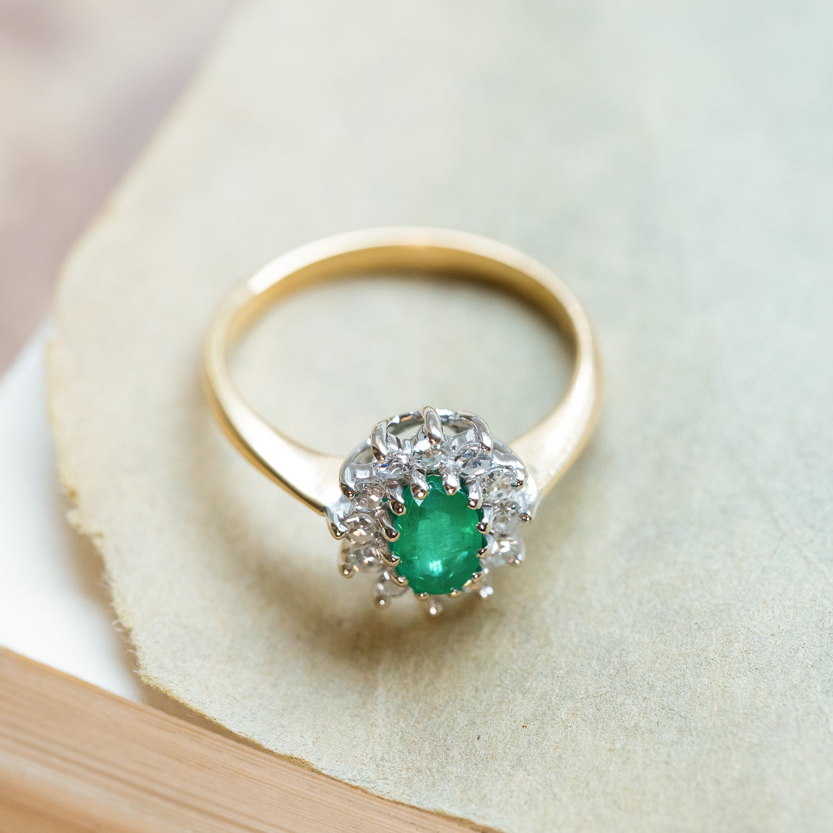 Vintage 1980s emerald and diamond cluster ring with yellow gold band and diamond surround.