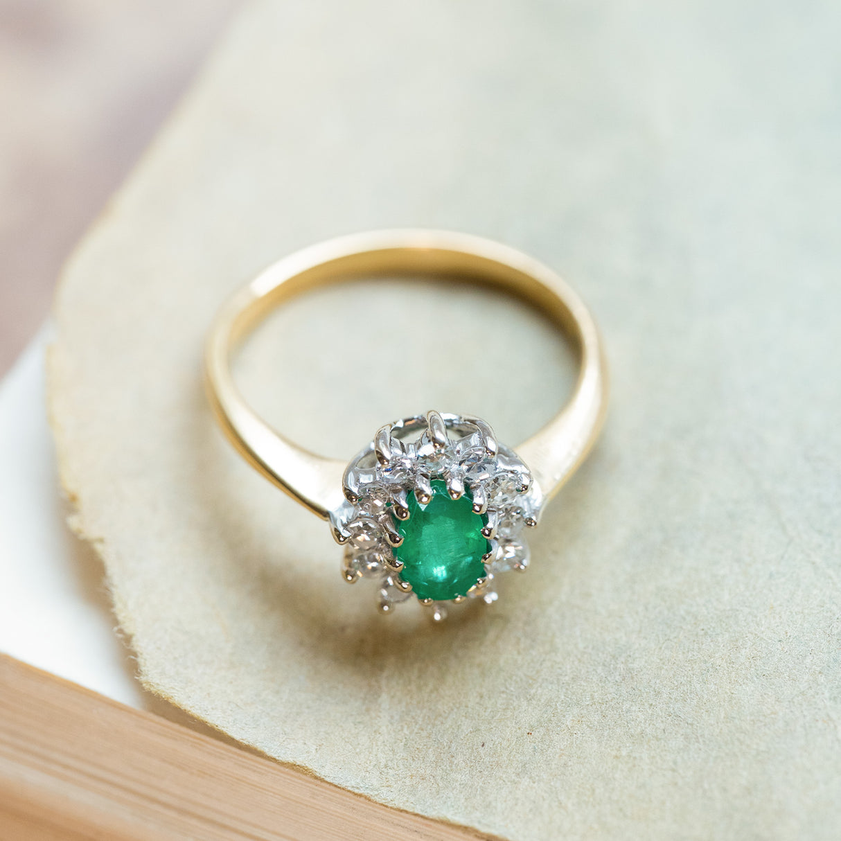 Vintage 1980s emerald and diamond cluster ring with yellow gold band and diamond surround.