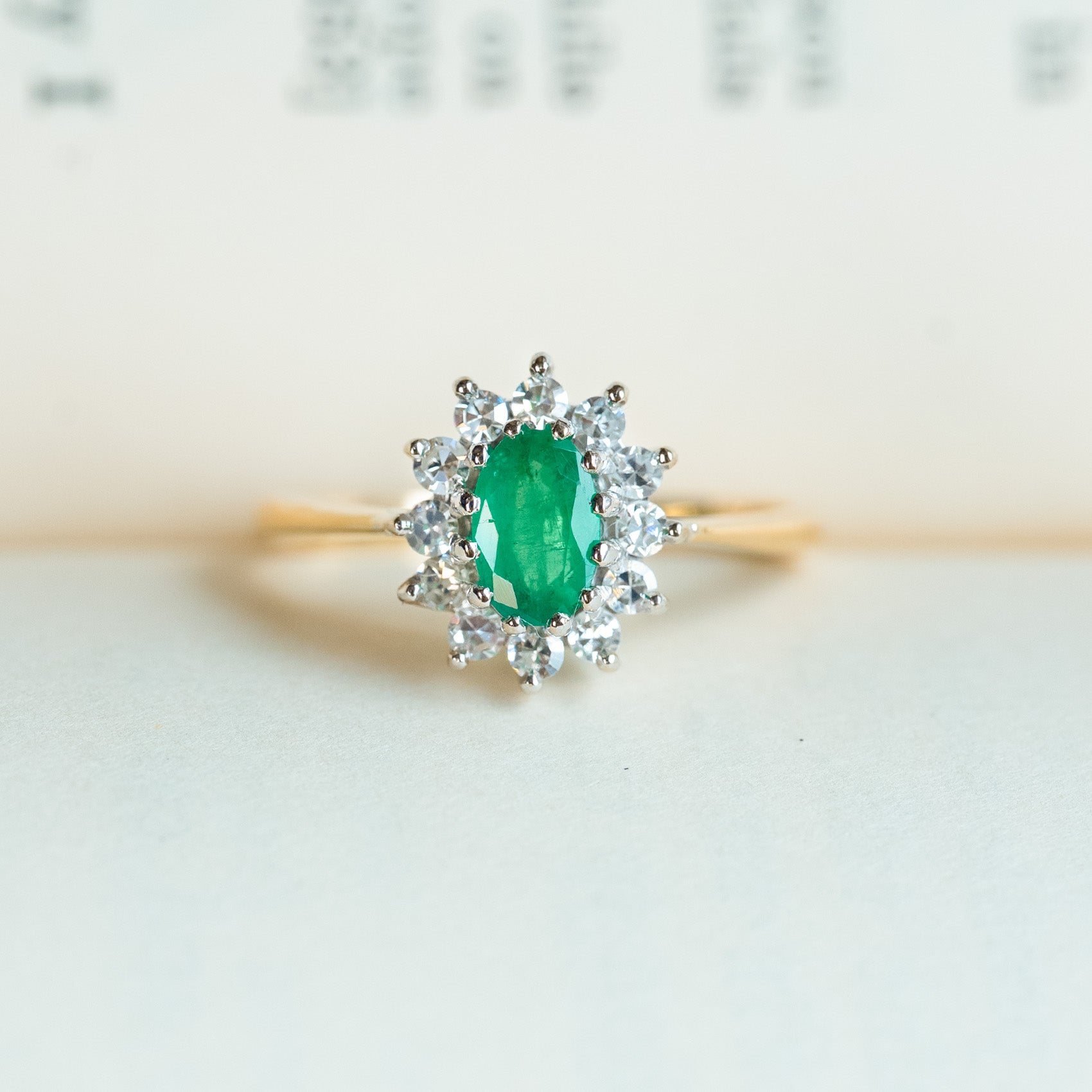 Vintage 1980s emerald and diamond cluster ring resting on paper background.