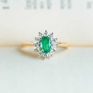 Vintage 1980s emerald and diamond cluster ring resting on paper background.