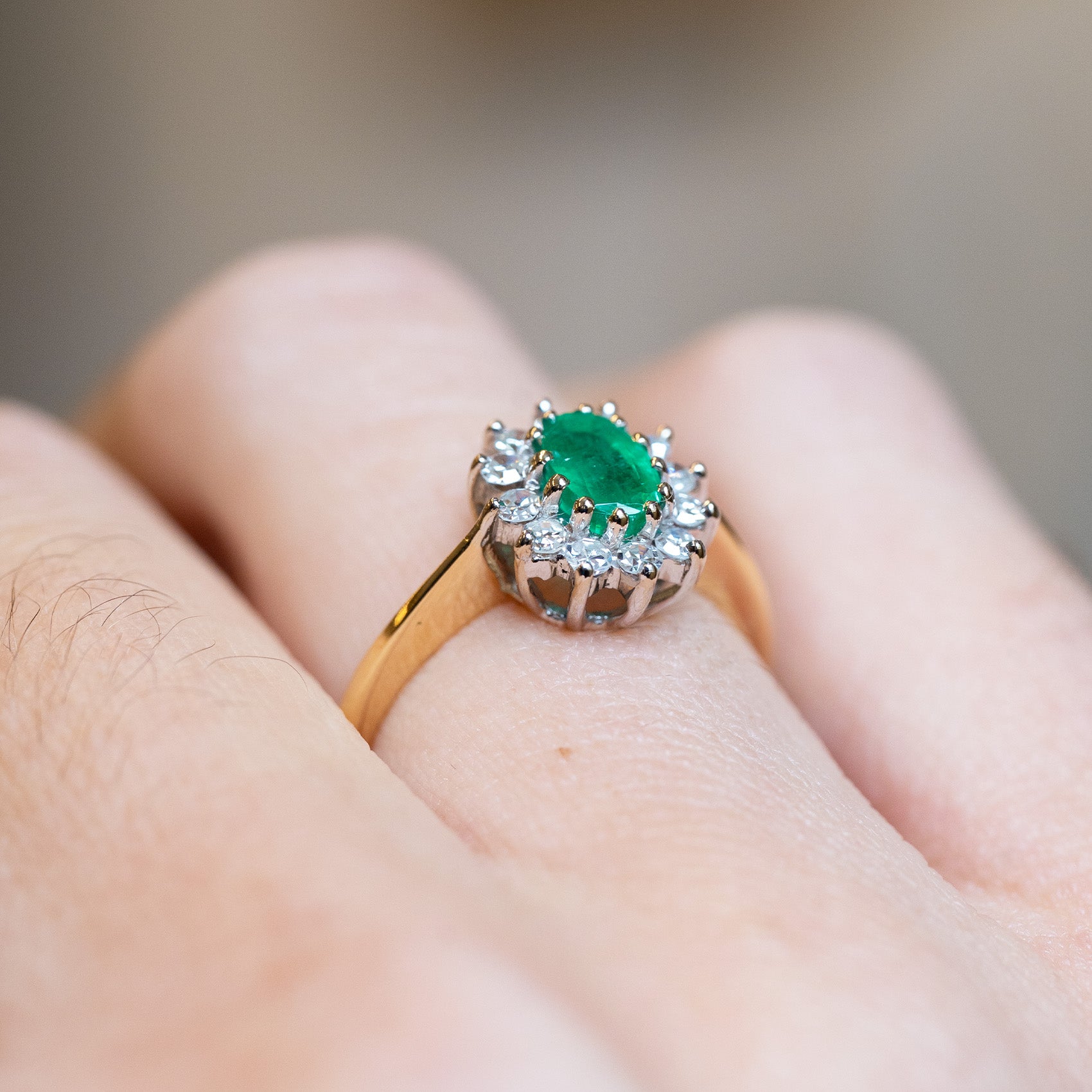 Vintage 1980s emerald and diamond cluster ring with raised diamond setting and yellow gold band.