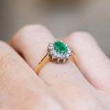 Vintage 1980s emerald and diamond cluster ring with raised diamond setting and yellow gold band.