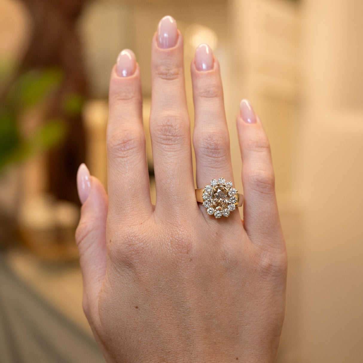 Vintage 1980s fancy coloured brown diamond cluster cocktail ring worn on the hand, featuring an oval brown diamond surrounded by brilliant-cut white diamonds in yellow gold.