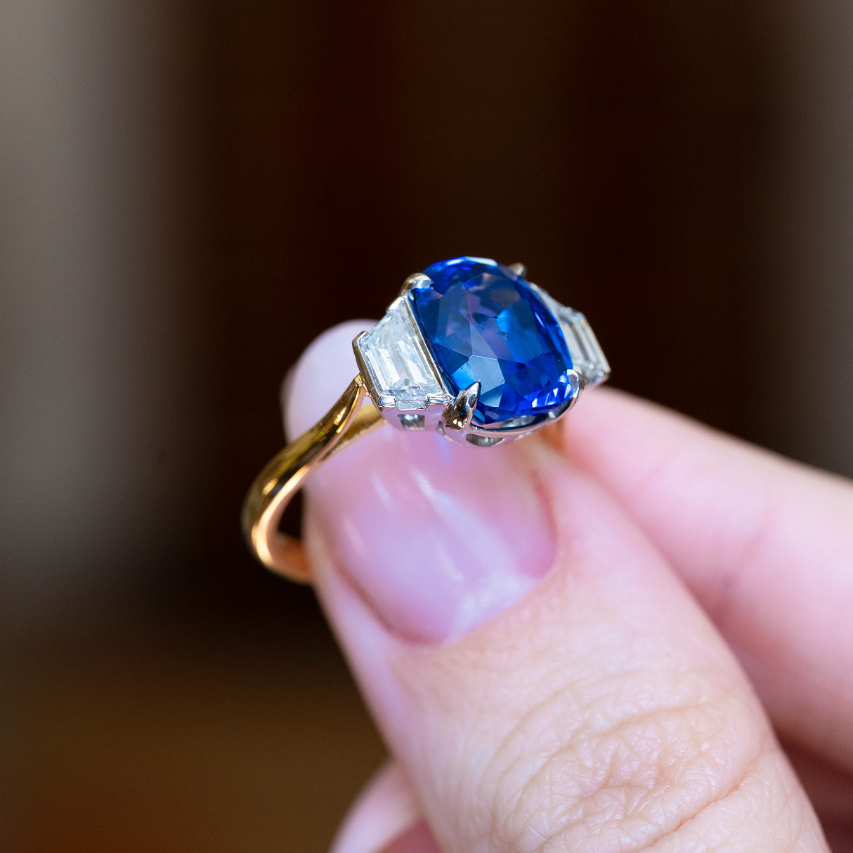 Vintage 1990s sapphire and diamond three-stone ring held between fingers showing vivid blue sapphire centre stone.