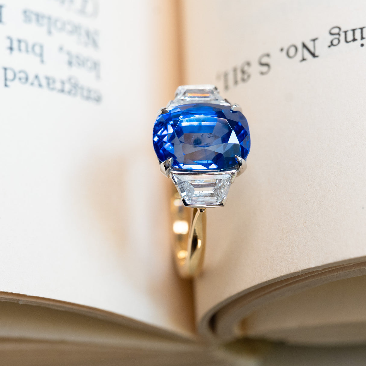 Vintage 1990s sapphire and diamond three-stone ring displayed between open book pages.