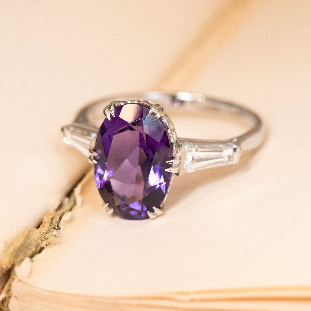Vintage amethyst and diamond three-stone ring showcasing an oval-cut purple amethyst with tapered baguette diamond shoulders in platinum.