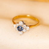 Vintage sapphire and diamond cluster ring showcasing a round blue sapphire framed by sparkling diamonds in a classic floral-inspired design.