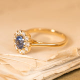 Vintage-inspired blue sapphire and diamond cluster ring showcasing a lively blue sapphire framed by brilliant-cut diamonds.