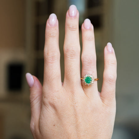 Vintage cluster ring worn on hand with vivid green centre stone and diamond cluster.