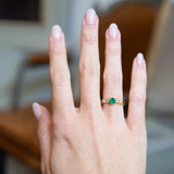 Vintage five stone ring worn on hand with central emerald and diamond accents.