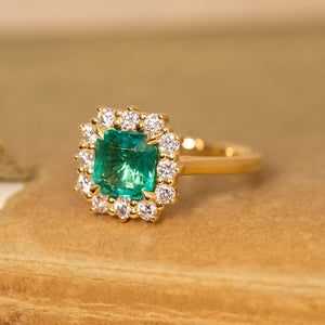 Vintage emerald and diamond halo engagement ring showcasing an emerald-cut emerald framed by a sparkling diamond cluster in yellow gold.