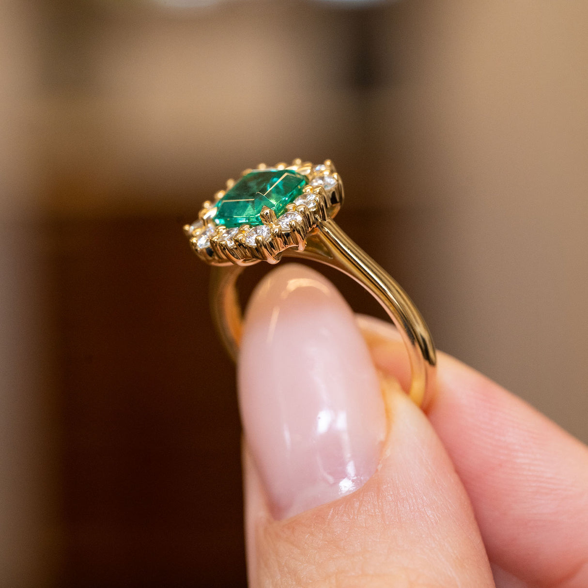 Vintage emerald and diamond halo engagement ring showcasing an emerald-cut emerald with a sparkling diamond cluster and yellow gold setting.