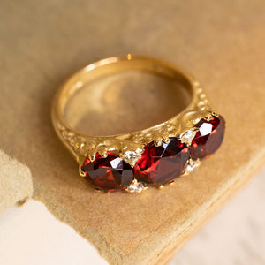 Vintage garnet and diamond ring with three oval garnets, decorative carved detailing and a classic half-hoop design.