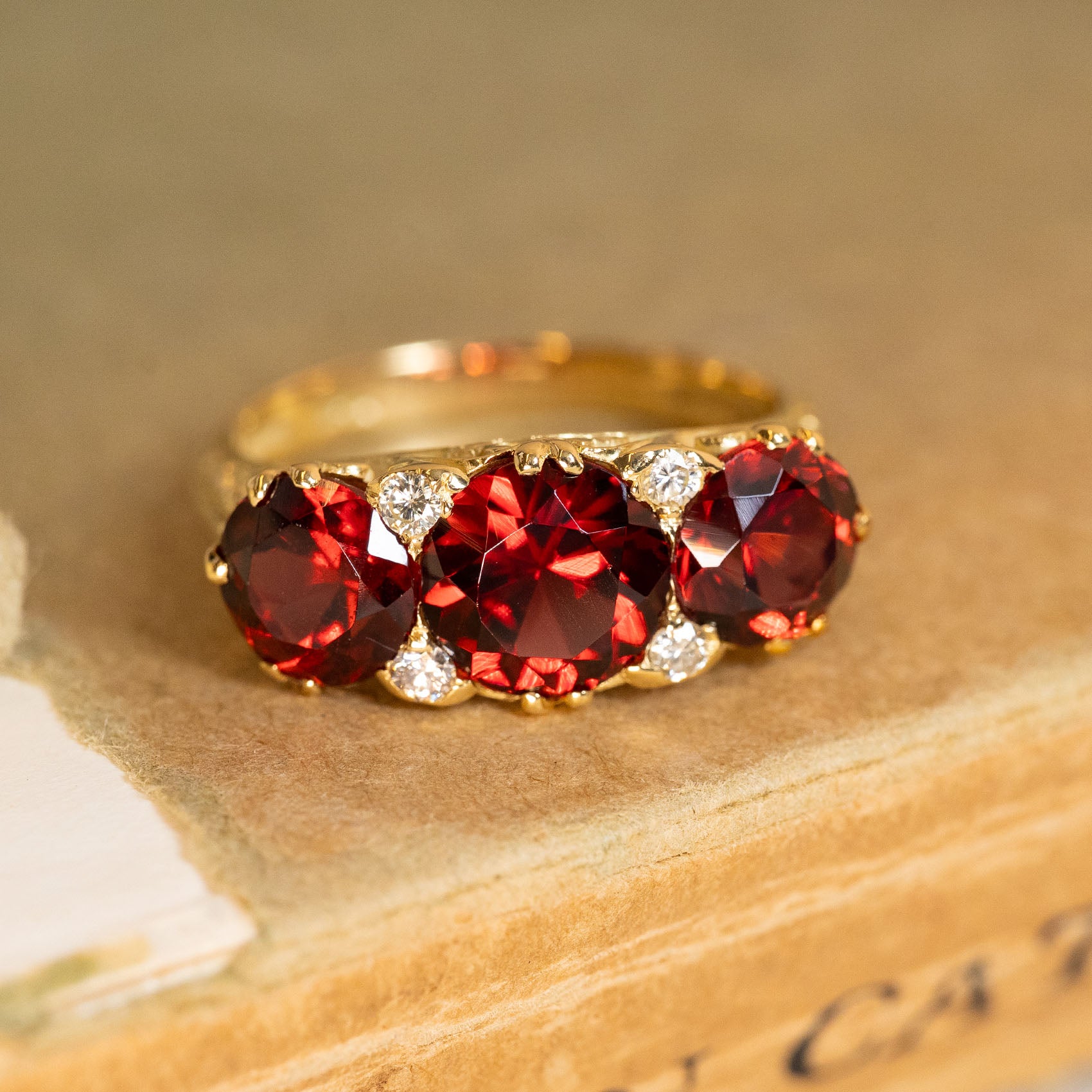 Vintage garnet three-stone half-hoop ring featuring richly coloured garnets accented by old-cut diamonds in yellow gold.