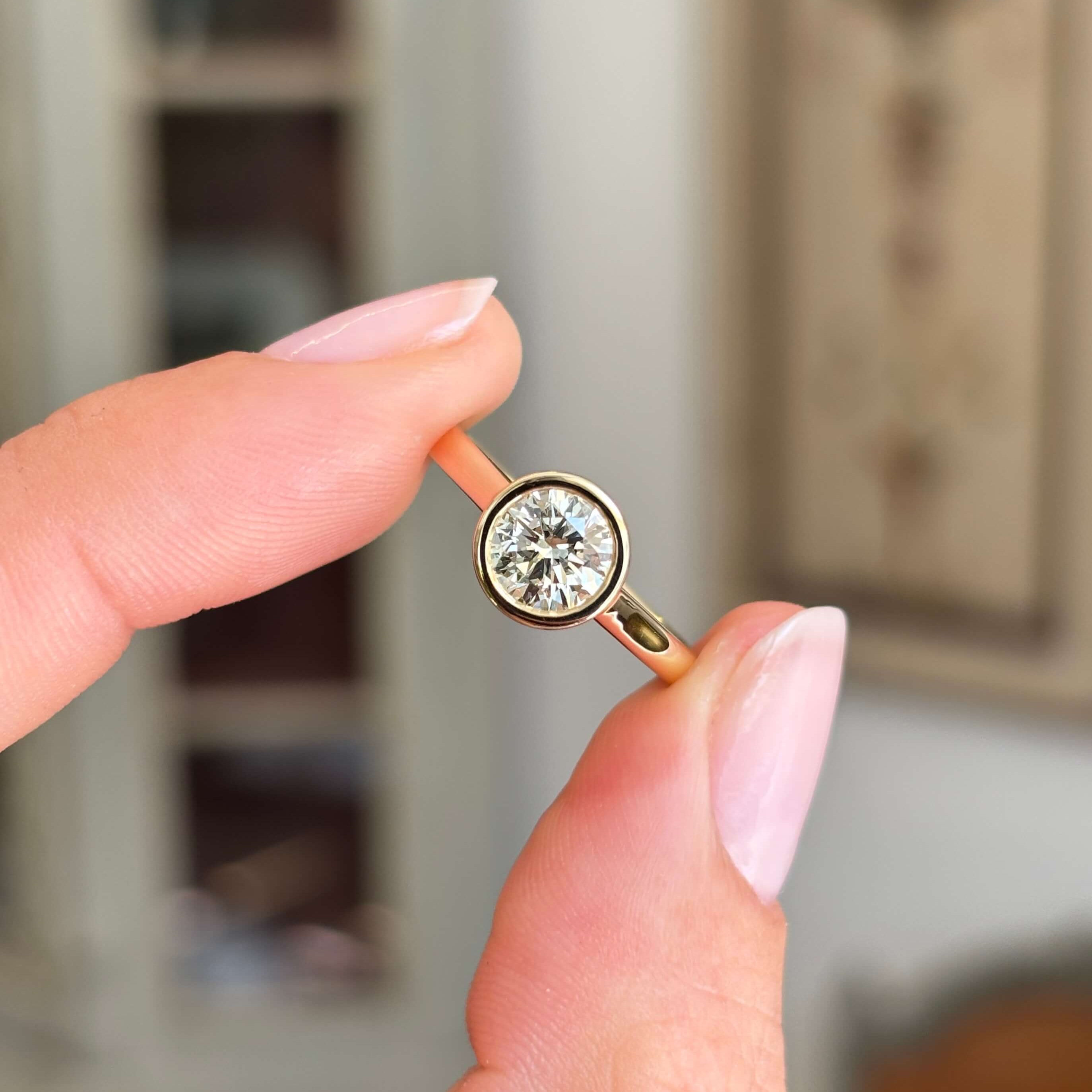 Vintage inspired diamond rub-over solitaire engagement ring with a round brilliant-cut diamond in a classic rub-over setting, held by hand.