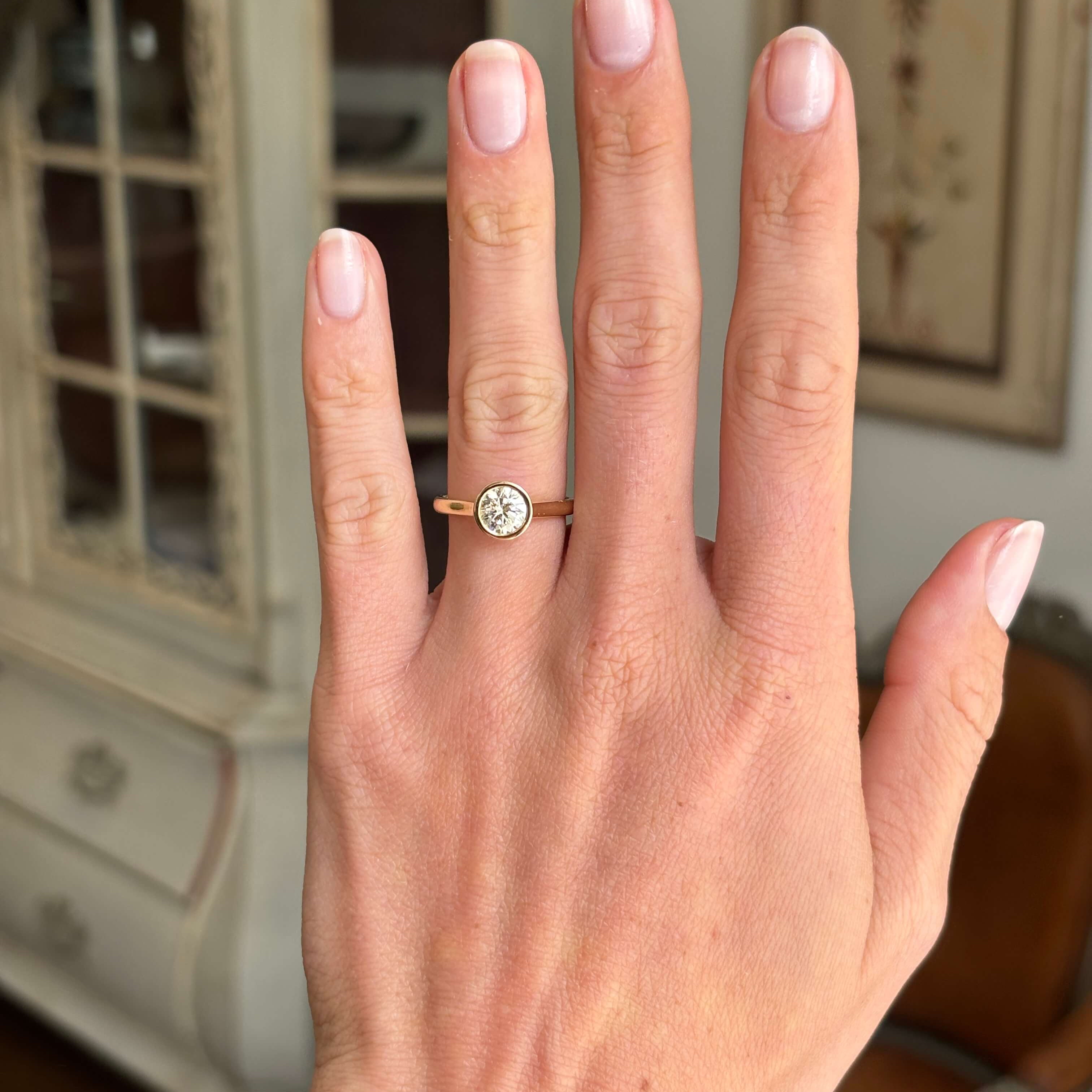 Vintage inspired diamond rub-over solitaire engagement ring featuring a round brilliant-cut diamond in a smooth rub-over setting, displayed on a hand.