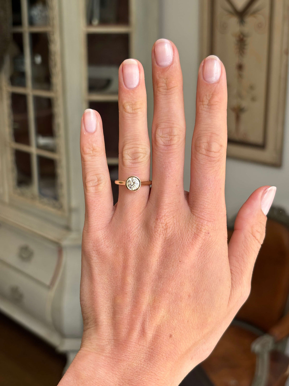 Vintage inspired diamond rub-over solitaire engagement ring featuring a round brilliant-cut diamond in a smooth rub-over setting, displayed on a hand.