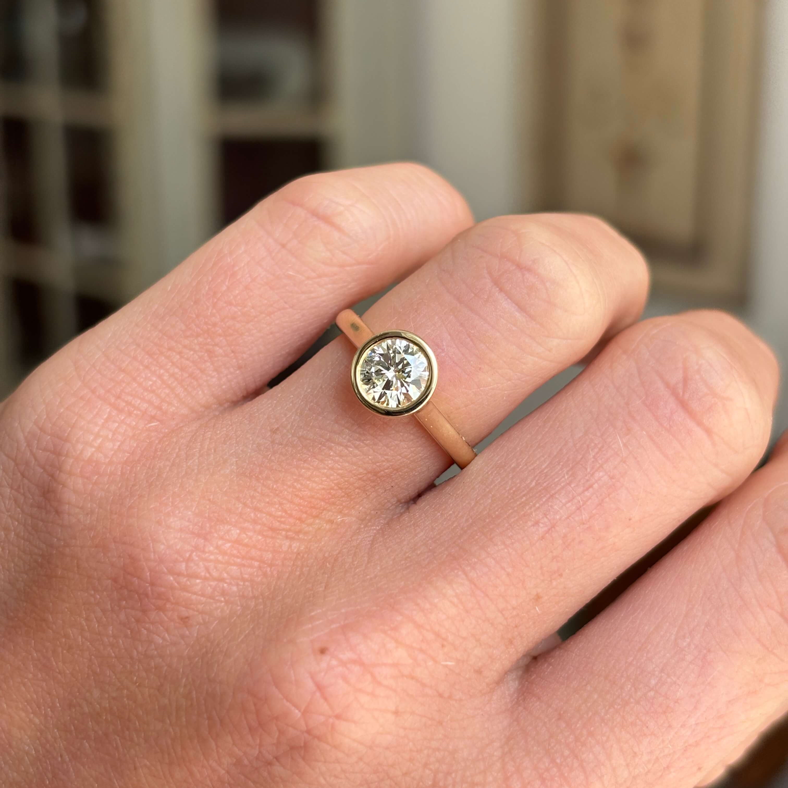 Vintage inspired diamond rub-over solitaire engagement ring with a round brilliant-cut diamond in a timeless rub-over setting, worn on a hand.