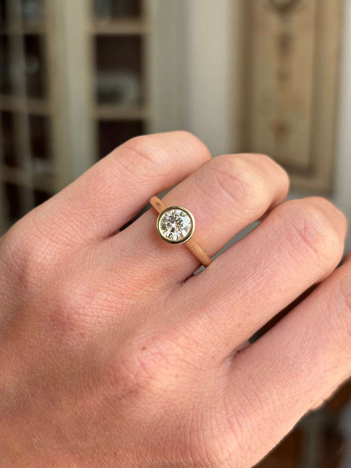 Vintage inspired diamond rub-over solitaire engagement ring with a round brilliant-cut diamond in a timeless rub-over setting, worn on a hand.