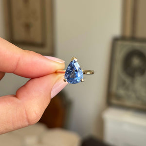 Vintage inspired pear-cut bluebell sapphire solitaire engagement ring featuring a pear-shaped bluebell sapphire in a classic yellow gold setting, held by hand.